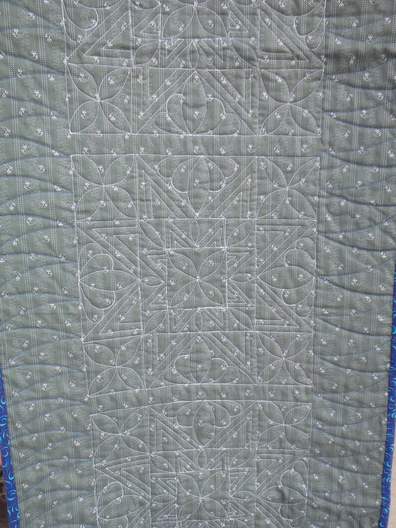 Puede incluir: Primer plano de una tela acolchada verde con un patr&oacute;n geom&eacute;trico blanco. La tela est&aacute; cosida con hilo blanco, creando un dise&ntilde;o detallado.