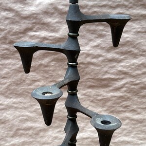 Può includere: Un candelabro in metallo nero con cinque portacandele a forma di albero stilizzato. Il candelabro ha una base rotonda e uno stelo alto e sottile.