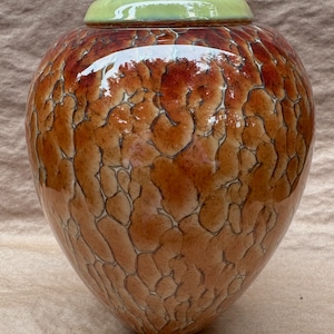 Könnte beinhalten: Eine braune Keramikvase mit einer craquelé-Glasur. Die Vase hat einen runden Körper und eine schmale Öffnung. Die Oberseite der Vase ist hellgrün.