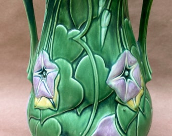 May include: Green ceramic vase with two handles, featuring a relief design of morning glory flowers and leaves. The flowers are lavender and yellow, set against a green background. The vase has a bulbous shape.