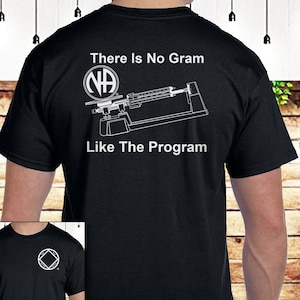Può includere: Maglietta nera con una grafica bianca di una bilancia con il testo "There Is No Gram Like The Program" e un simbolo NA bianco. Il simbolo NA è un cerchio con le lettere NA all'interno.