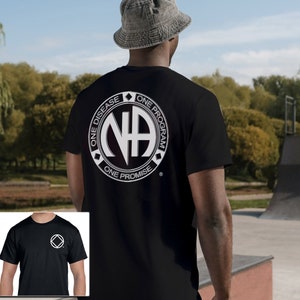 May include: Black t-shirt with a white circle logo that says "One Disease, One Program, One Promise" and has the letters "NA" in the center. The logo is on the back of the shirt. A smaller black t-shirt with a white "NA" logo is shown in the bottom left corner.