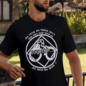 May include: Black t-shirt with a white graphic of handcuffs in a diamond shape. The text "As long as these ain't the ties that bind us together... All Will Be Well!" is printed on the shirt.