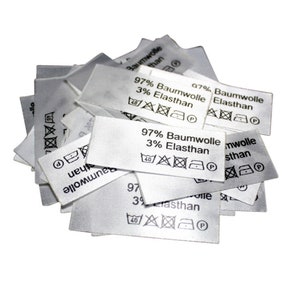 Könnte beinhalten: Ein Stapel weißer Stoffpflegeetiketten mit schwarzem Text und Symbolen. Die Etiketten geben an, dass der Stoff aus 97 % Baumwolle und 3 % Elasthan besteht. Die Symbole zeigen Anweisungen zum Waschen, Trocknen, Bügeln und Bleichen.