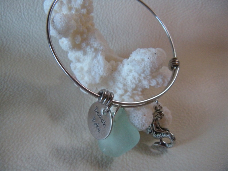 May include: Silver charm bracelet with a mermaid charm, a sea glass charm, and a charm that says "Beach Babe".