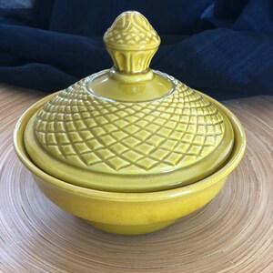 May include: A yellow ceramic bowl with a lid. The lid has a decorative knob on top and a diamond pattern.