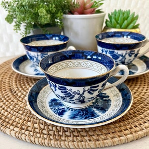 May include: Set of three blue and white porcelain teacups and saucers with a gold trim. The cups and saucers feature a traditional Chinese willow pattern.