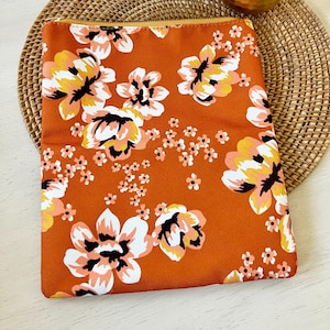 May include: A rust-colored zippered pouch with a floral print featuring white, pink, and yellow flowers on a rust-colored background.