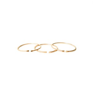 May include: Three gold-toned rings, each with a slightly different diameter, are stacked on top of each other. The rings are simple and minimalist in design, with a smooth, polished finish.