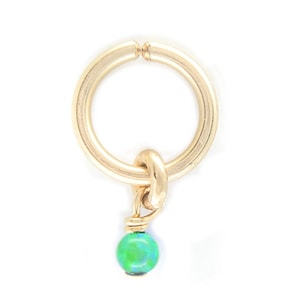 Puede incluir: Un amuleto de oro con una cuenta de &oacute;palo verde que cuelga de un anillo de oro.