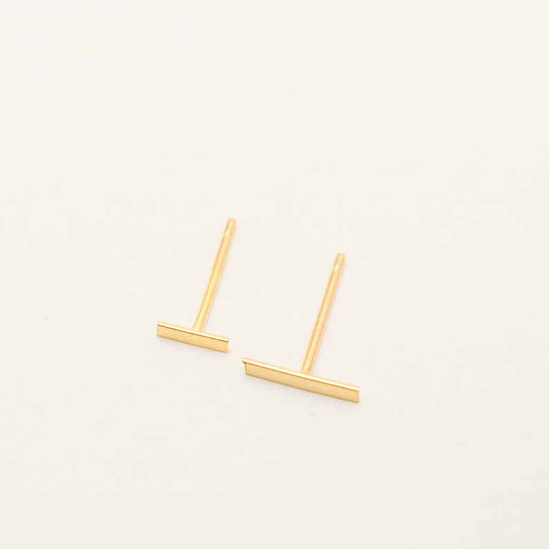 Op de afbeelding: Een paar gouden staaf oorbelletjes. De oorbelletjes zijn simpel en minimalistisch, met een dun staafje ontwerp.