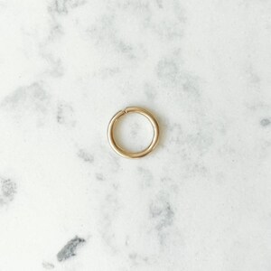 Polished gold hoop with a small opening, lying on a white and gray marble surface, seen from above.