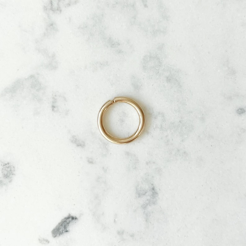 Polished gold hoop with a small opening, lying on a white and gray marble surface, seen from above.