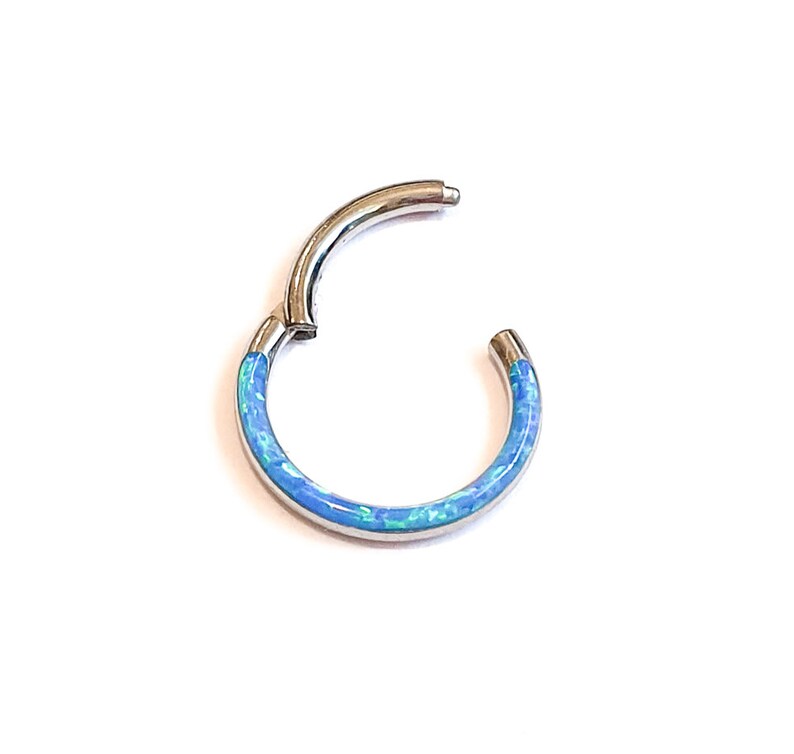 May include: A silver hoop earring with a blue opal inlay. The hoop is seamless and has a hinged closure.