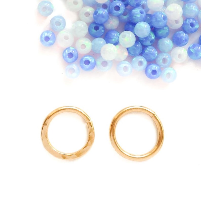 Two gold hoops side by side on white, one hammered and one polished, with a pile of blue and white beads above them.