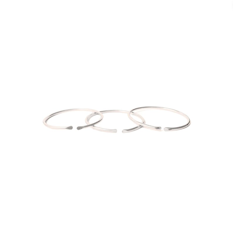 May include: Three silver rings, each with a slightly different diameter, are stacked on top of each other. The rings are simple and minimalist in design.