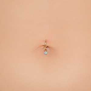 Puede incluir: Un piercing de ombligo de oro con un peque&ntilde;o colgante de &oacute;palo.