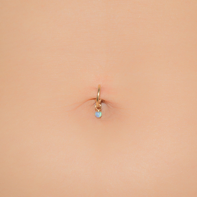 Puede incluir: Un piercing de ombligo de oro con un peque&ntilde;o colgante de &oacute;palo.