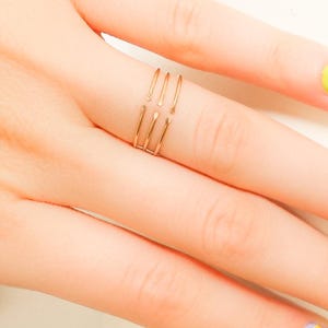 Könnte beinhalten: Ein goldfarbener Ring mit vier dünnen Bändern, die oben verbunden sind. Der Ring wird an einem Finger getragen.