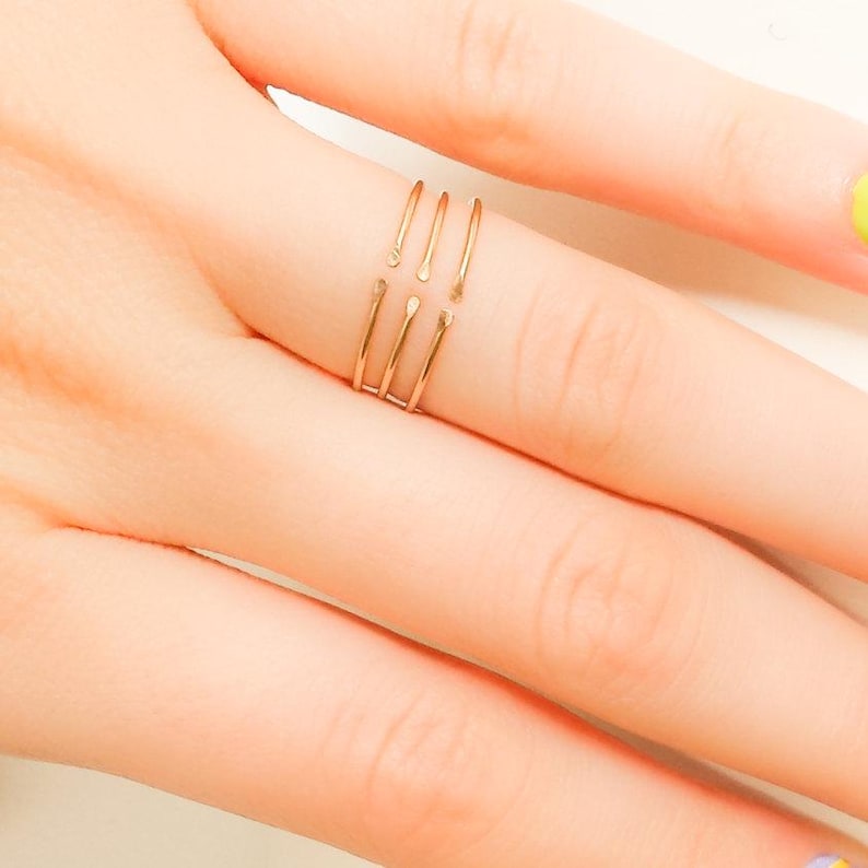 May include: A gold-toned ring with four thin bands that are connected at the top. The ring is worn on a finger.