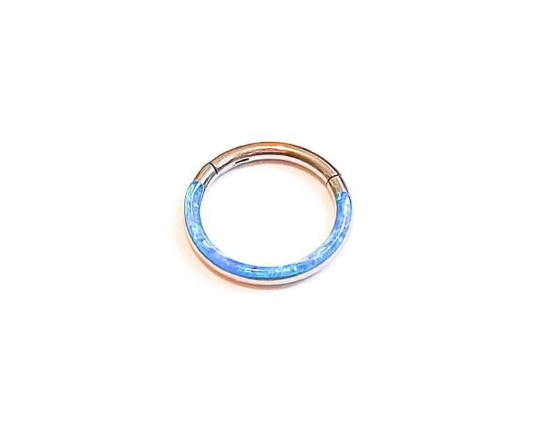 May include: A silver ring with a blue opal inlay. The ring is a seamless hoop with a hinged closure.