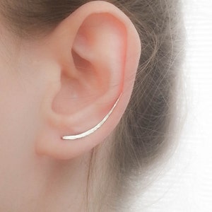 May include: A silver ear cuff with a hammered finish. The cuff is curved and sits on the upper part of the ear.