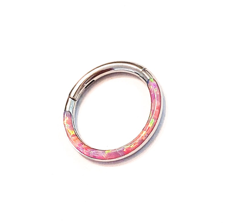May include: A silver ring with a pink and white opal inlay. The ring is a seamless hoop with a hinged closure.