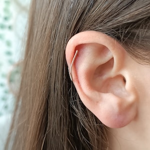 Op de afbeelding: Een close-up van een oor met een kleine, zilveren oorring in de bovenste kraakbeenpiercing.