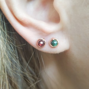 Peut inclure: Une paire de petites boucles d'oreilles à clous avec une pierre précieuse rouge dans une oreille et une pierre précieuse verte dans l'autre. Les boucles d'oreilles sont serties dans un métal doré.