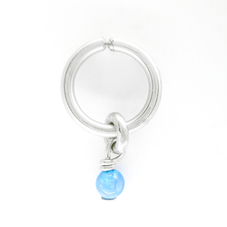 Puede incluir: Un charm plateado con una cuenta de vidrio azul claro unida a &eacute;l. El charm tiene la forma de un c&iacute;rculo con una peque&ntilde;a abertura.