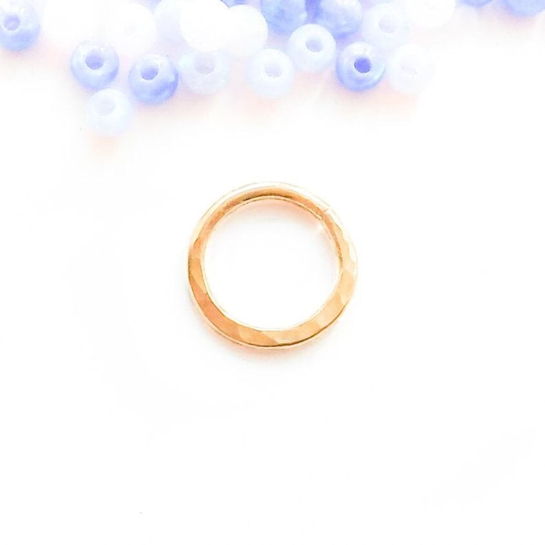 Hammered gold hoop lying flat on a white surface, with pale blue and white beads scattered at the top of the frame.