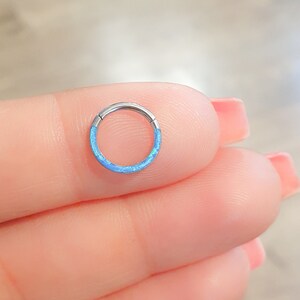 May include: A small, silver hoop earring with a light blue opal inlay. The hoop is seamless and has a polished finish.