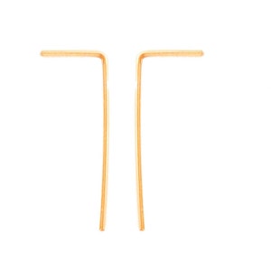 May include: A pair of gold-toned earrings with a simple, minimalist design. Each earring is a thin, straight piece of metal that is bent at a right angle to form a small, angled shape.