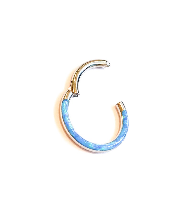 May include: A silver hoop earring with a blue opal inlay. The hoop is open and ready to be worn.