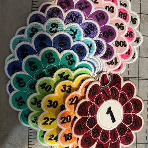 May include: A set of colorful flower-shaped fabric patches with numbers 1 through 72. The patches are arranged in a circle, with the number 1 in the center.