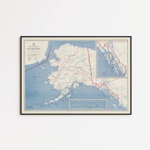 May include: A framed vintage map of Alaska, displaying detailed geographical information. The map has a blue and beige colour scheme with red border lines. The word "ALASKA" is printed at the top left corner. The map is enclosed in a black frame.