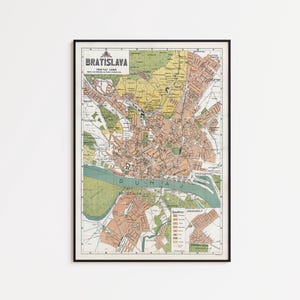 Op de afbeelding: Een ingelijste vintage kaart van Bratislava, Slowakije, met een raster, de rivier de Donau aangeduid als Dunaj, en diverse stedelijke sectoren in tinten perzik, geel en groen. De titel Bratislava staat in de linkerbovenhoek gedrukt.