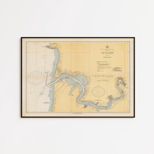 May include: A framed nautical chart titled Yaquina River and Approaches, featuring a tan background with blue water details, black text, and navigational markings. The map displays coastal geography, depth soundings, and a compass rose.
