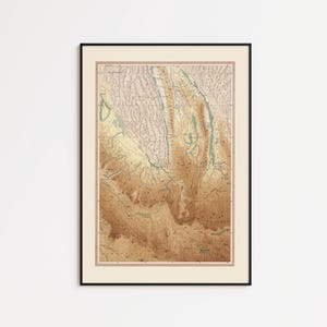 Op de afbeelding: Ingelijste vintage kaartprint met een gedetailleerd topografisch beeld in bruin-, beige- en groentinten. De kaart zit in een zwart frame met een crèmekleurige passe-partout. Ideaal voor thuis of op kantoor.