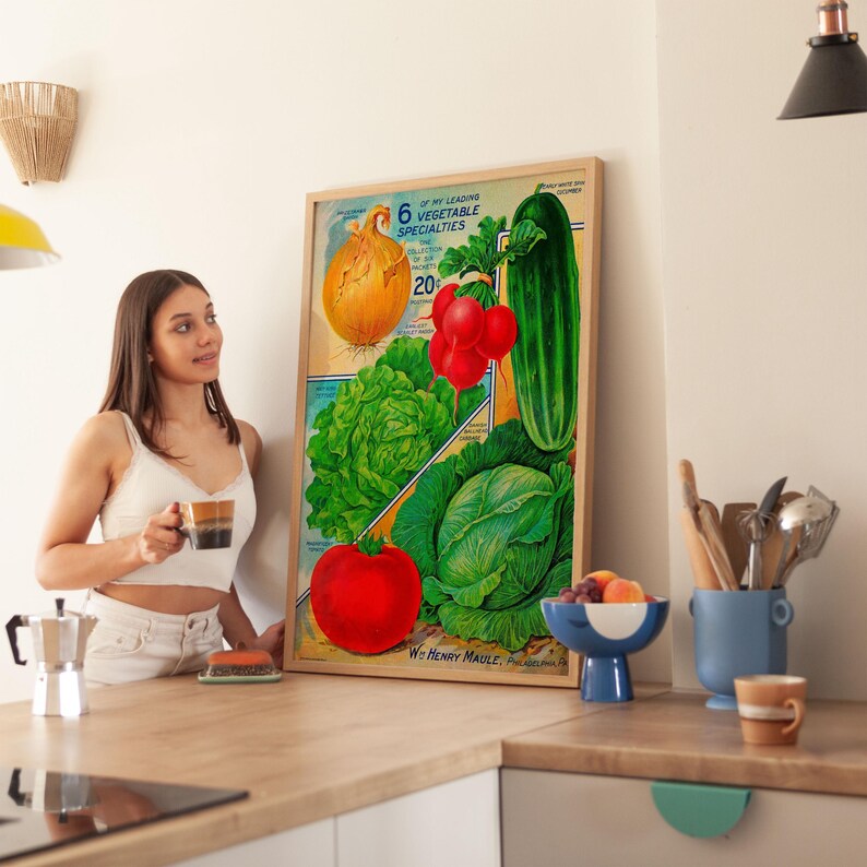 May include: A framed vintage print featuring illustrations of six vegetables: an onion, radishes, a cucumber, lettuce, a cabbage, and a tomato. The print has a beige background with text that reads "6 of the Leading Vegetable Specialties".