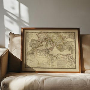 K&ouml;nnte beinhalten: Eine gerahmte Karte im antiken Stil der Mittelmeerregion mit detaillierten K&uuml;stenlinien, geografischen Bezeichnungen und historischen kartografischen Markierungen in ged&auml;mpften Beige- und Braunt&ouml;nen, eingefasst in einen schlichten dunklen Holzrahmen.