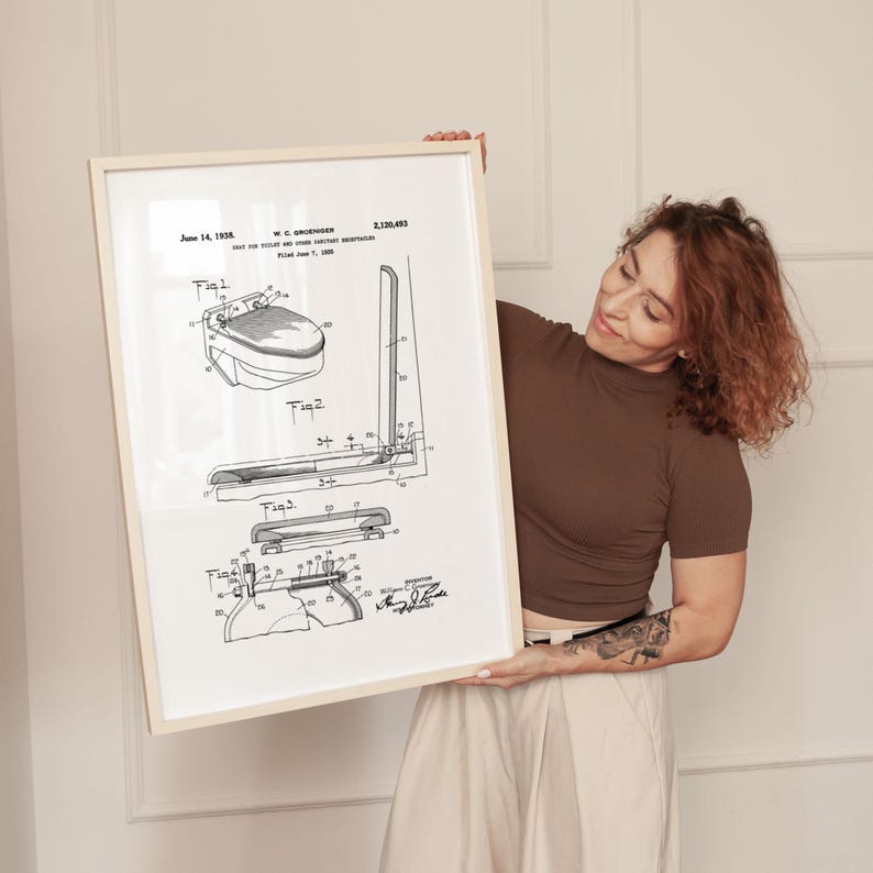 May include: A framed black and white patent print of a toilet, dated June 14, 1938. The print includes detailed diagrams and technical drawings of the toilet's components. The frame is a light beige color.