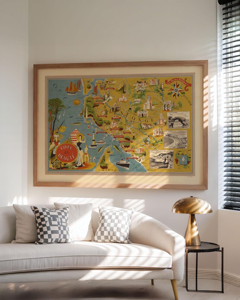 May include: A framed vintage-style map print titled Cote de Beaute, featuring a yellow and blue illustrated coastal landscape with ships, lighthouses, and small inset black and white photographs, enclosed in a light-toned wooden frame.