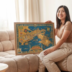 May include: A framed vintage map of Newport, Rhode Island, in a wooden frame. The map features a detailed illustration in shades of blue, yellow, and brown, with the text "NEWPORT RHODE ISLAND" at the bottom. The map is held by a person.