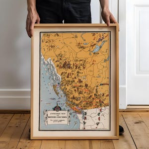 May include: A framed vintage-style illustrated map of British Columbia with a tan landmass and blue coastal waters. The map features various small drawings of wildlife, activities, and landmarks, with the text "ANIMATED MAP OF BRITISH COLUMBIA".