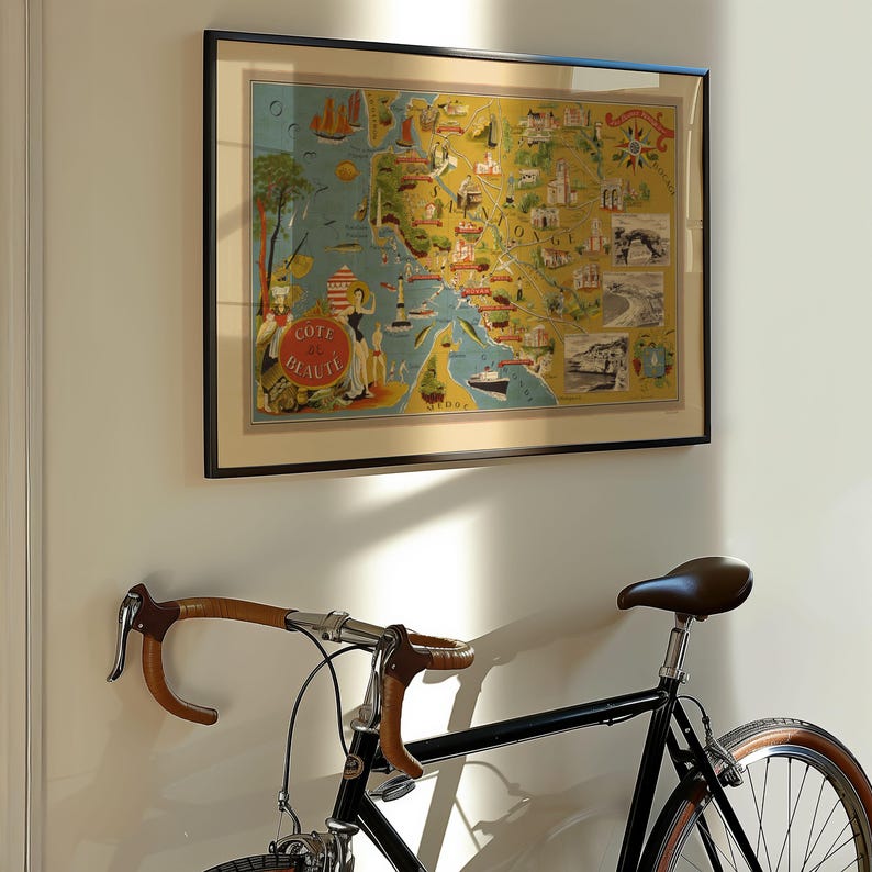 May include: A framed vintage-style map print titled Cote de Beaute featuring yellow and blue coastal illustrations, landmarks, and a compass rose. The artwork is displayed in a thin black frame above a black bicycle with brown handlebars.