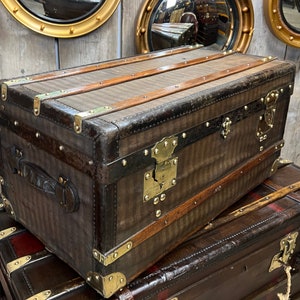 Puede incluir: Un ba&uacute;l marr&oacute;n vintage con herrajes de lat&oacute;n y detalles de cuero. El ba&uacute;l presenta un patr&oacute;n de rayas en la parte delantera y superior, con protectores de esquina de lat&oacute;n y una cerradura central. El ba&uacute;l es rectangular.