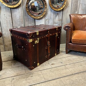 Handmade in England leather steamer trunk with full brass fittings, stud edging and leather straps on a polished white floor