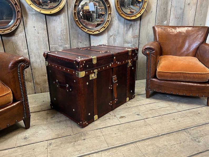 Handmade in England leather steamer trunk with full brass fittings, stud edging and leather straps on a polished white floor