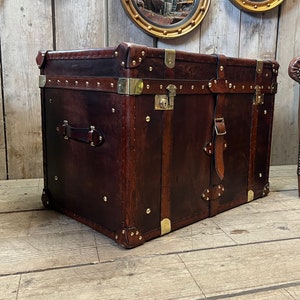 Dark hand dyed leather trunk with brass stud trim, corner plates and buckled carry straps, used as a coffee table chest